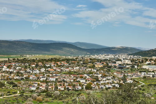 Preview: A panoramic view of a rural town nestled among rolling green hills, under a bright blue sky
