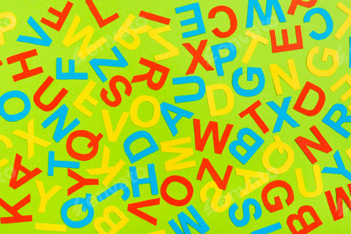 Preview: Multicolored letters of the English alphabet cut out of cardboard laid out randomly on a green