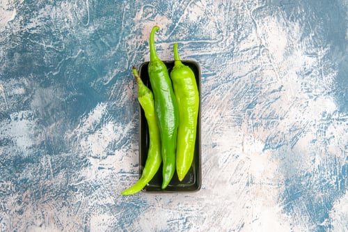 Preview: top view green hot peppers on black plate on blue-white background with copy space