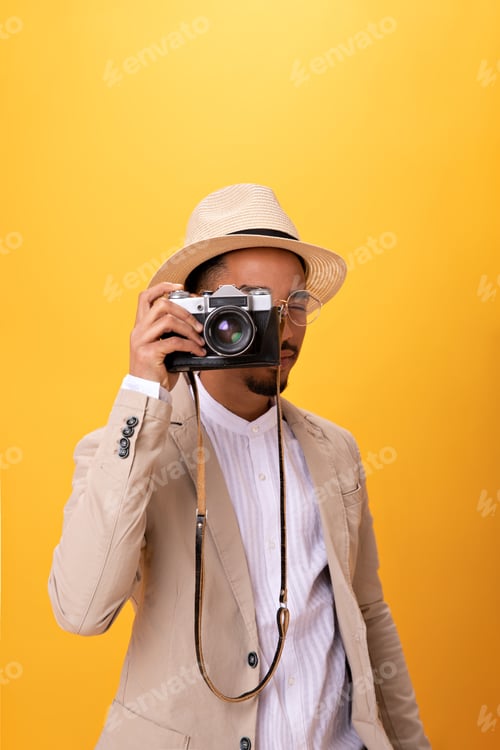 Preview: Portrait of man in beige suit taking photo on retro camera. Charming guy in white tee and hat posin