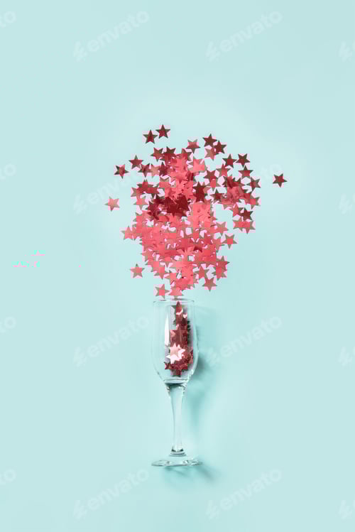 Preview: Red confetti in shape of stars poured out glasses of champagne on blue.