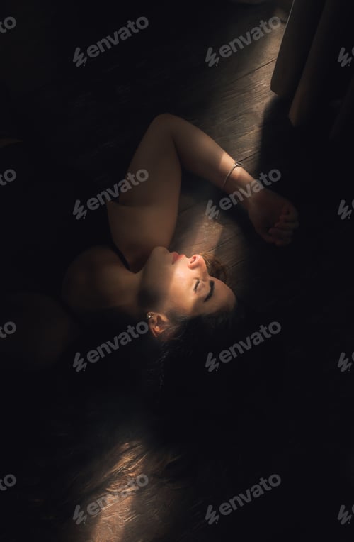 Preview: Vertical shot of a Caucasian female lying on the floor in a dark room with sunrays illum