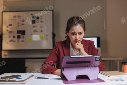 Preview: Businesswoman thinking intently looking at data on tablet
