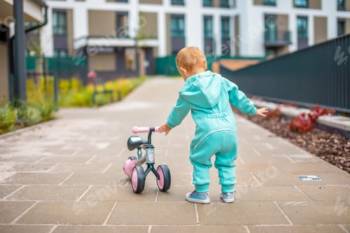 Preview: Cute little toddler girl in blue overalls riding on run balance bike. Happy healthy lovely baby chil