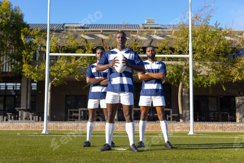 Preview: Three African American young male athletes holding a rugby ball on a field outdoors