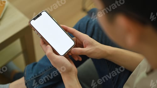 Preview: Close up view of man hands holding mobile phone, sitting on couch at home.