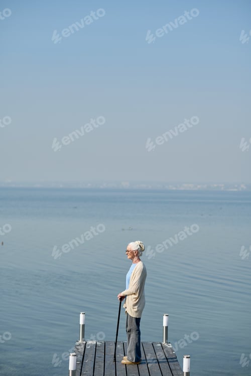 Preview: Long shot of retired woman with walking cane standing by lake