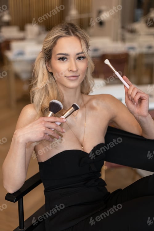 Preview: Beautiful fresh happy young girl with make up brushes sitting in beauty studio. Make up artist woman