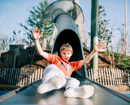 Preview: Preteen Boy Coming Out of a Tunnel Slide with his hands up and no shoes on on a bright sunny day