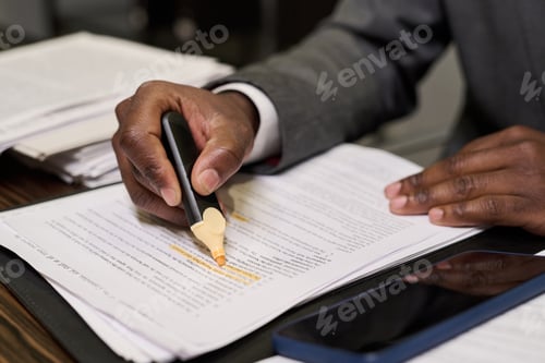 Preview: Black Man Highlighting Text on Document While Working at Desk