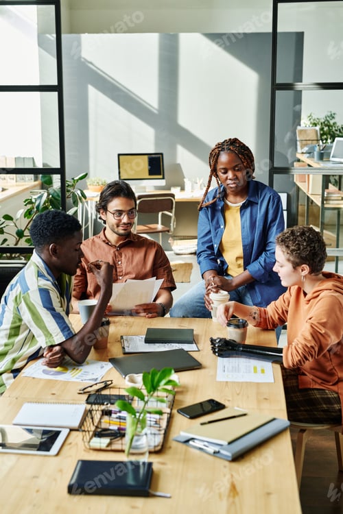 Preview: Group of young employees gathered by table in office