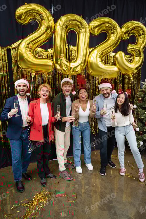 Visualização: Empresários multiculturais positivos em chapéus de Papai Noel segurando champanhe perto de balões em forma de 2023