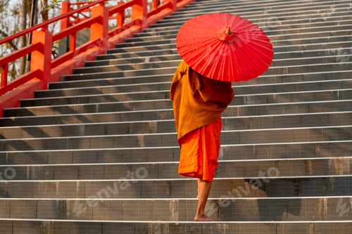 Preview: Close up back of monk with red umbrella walk on stair up to big buddha statue.