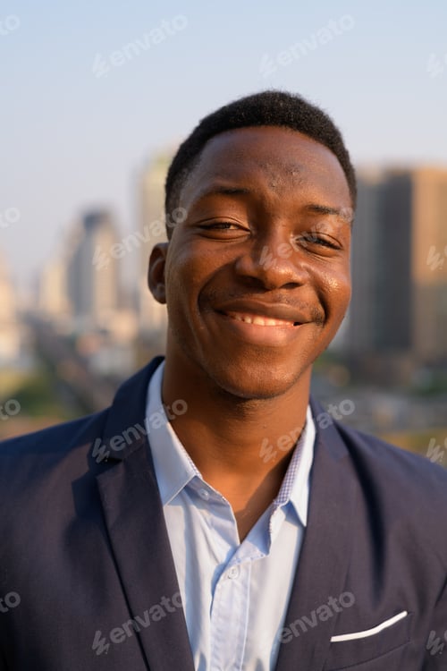 Preview: Face of young happy African businessman smiling against view of the city