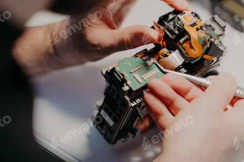Preview: Hands of handyman repairing broken digital camera, holds special tweezers, works in workshop