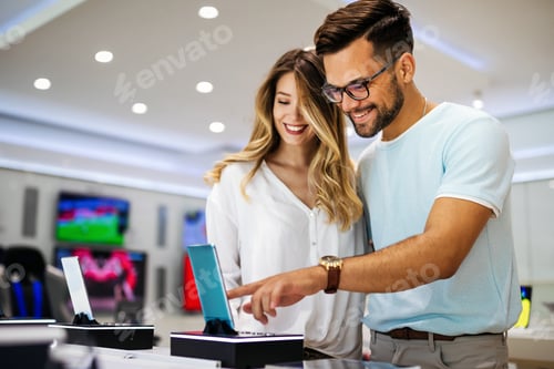 Preview: Young satisfied couple testing the new model of a smart cell phone from the desk in the tech store.
