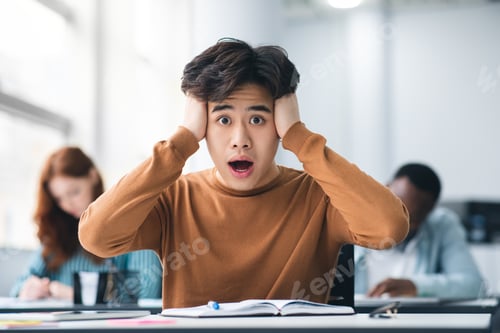 Preview: Asian male student grabbing head sitting at desk in class