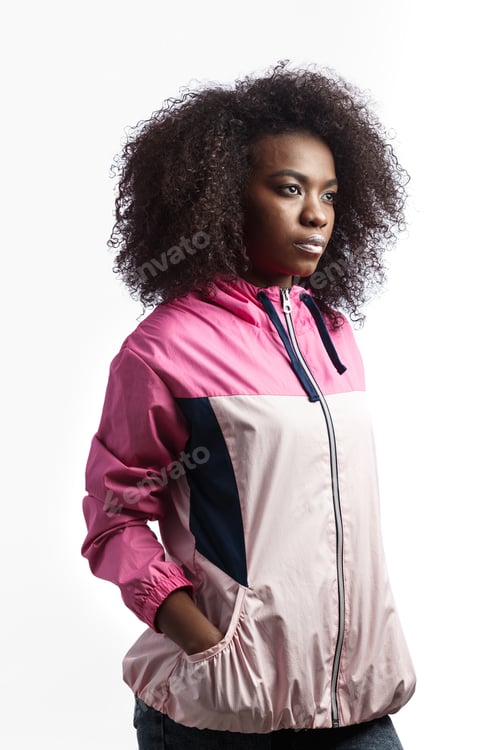 Preview: Young curly brown-haired girl dressed in the pink sport jacket stands at the white background in the