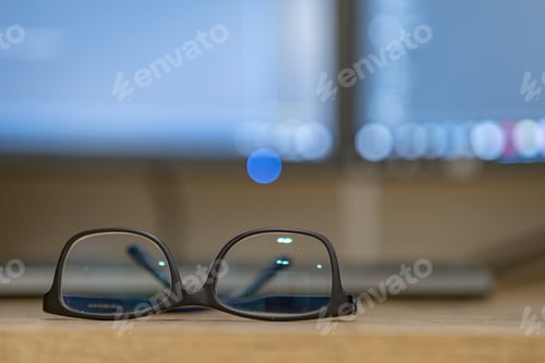 Preview: Closeup of protective glasses on an empty desk with blurred computer screen on background.