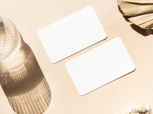 Preview: Two blank white cards, dry palm leaf, stone and glass of water on beige background top view