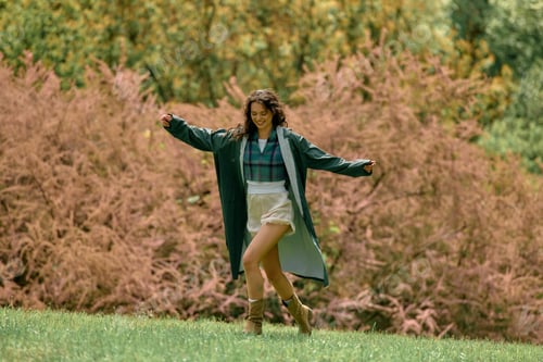 Preview: Stylish young woman twirls in a chic raincoat among lush greenery on a summer day