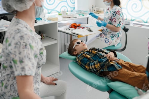 Preview: Little patient at the dentist. Dental hygienist cleans the teeth with the help of an assistant