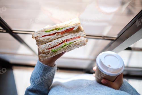 Preview: Top view image of a woman holding and eating whole wheat sandwich and coffee in the morning