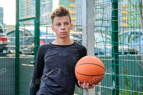 Preview: Guy teenager with basketball in his hands, outdoor basketball city court background