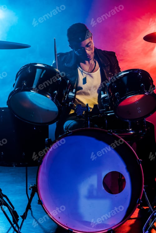Preview: handsome male musician in leather jacket playing drums during rock concert on stage with smoke and