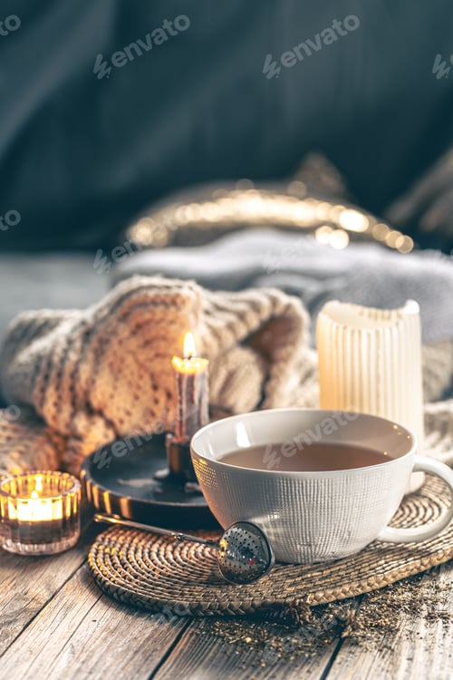 Preview: Cozy home composition with a cup of tea, candles and a knitted element.