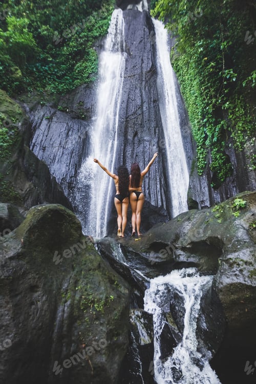 Preview: Two slim women relaxing near beautiful waterfall in Bali jungle. Nature adventure Dusun Kuning