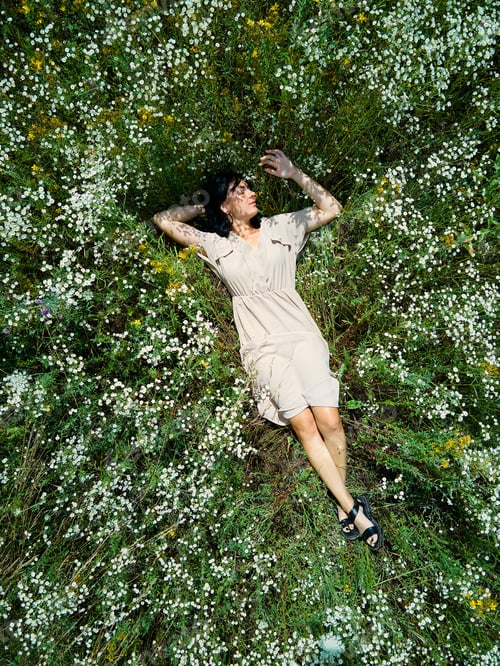 Preview: Drone aerial view of relax woman in dress lying on flower blooming meadow