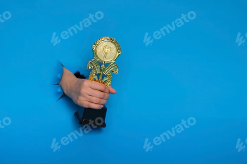 Preview: image of trophy in hand, concept for winning or success. Golden trophy on blue background, top view