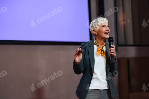 Preview: Senior woman explaining new business ideas to the audience, holding glasses.