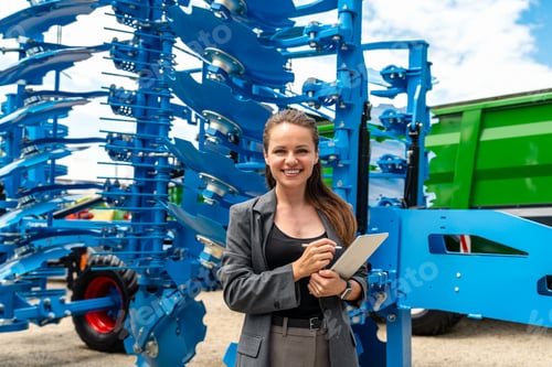 Preview: Modern businesswoman with tablet standing in front of farm implements at equipment dealership
