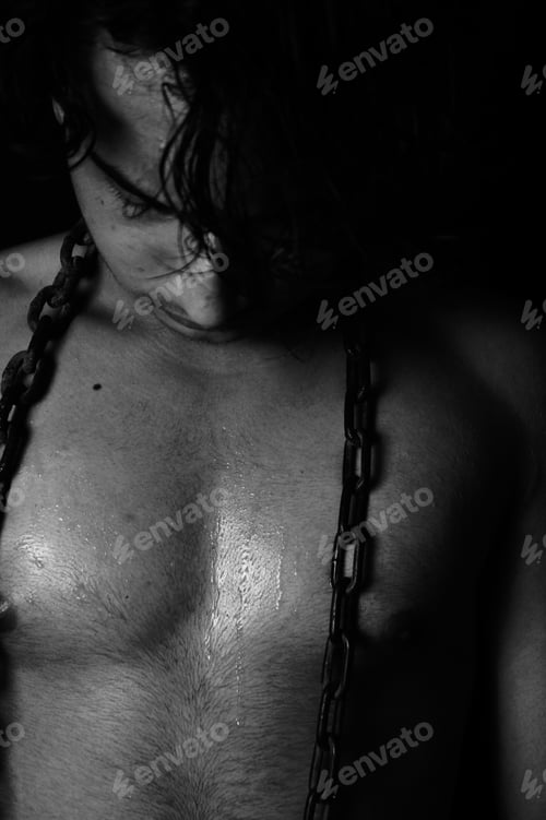 Preview: Vertical shot of a naked asian man with a metal chain around his neck in grayscale