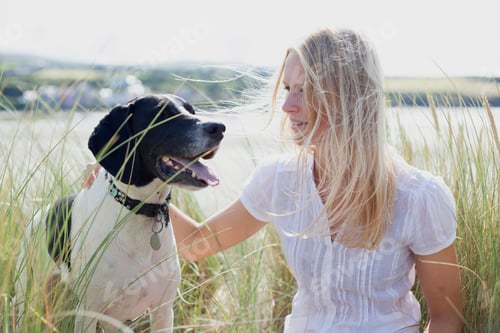 Preview: Smiling woman enjoying time with her happy dog in a sunny field.