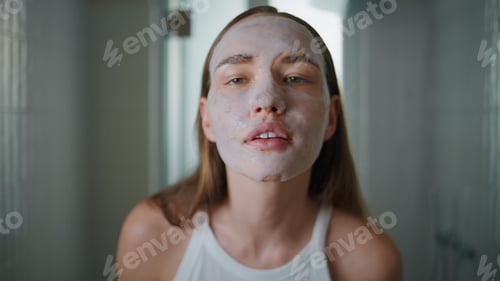 Preview: Girl wearing facial mask in bathroom closeup. Pretty model moisturizing skin