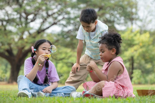 Preview: Children sitting in the park with blowing air bubble, Surrounded by greenery and nature