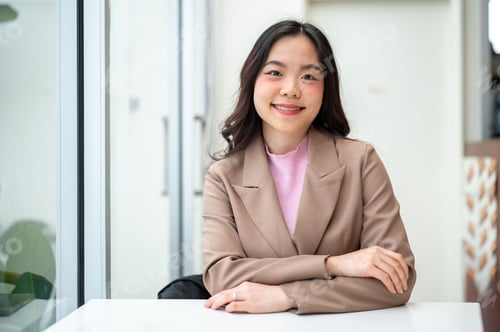 Preview: Pretty asian business woman or office worker sitting leisurely at white table in cafe or coffeeshop.
