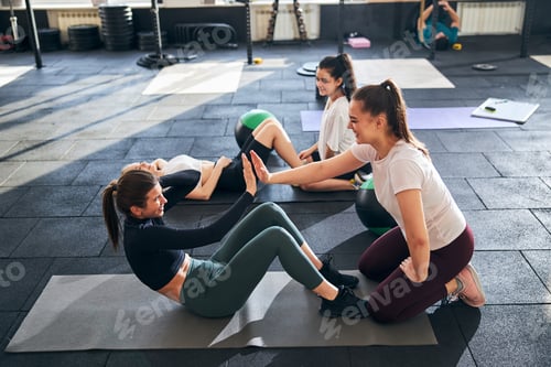 Preview: Young fit women doign sit-ups together at gym