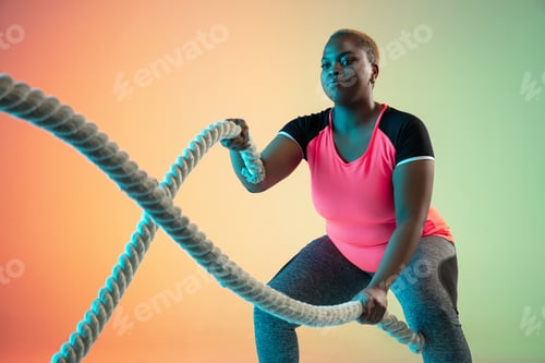 Preview: Young african-american plus size female model's training on gradient background
