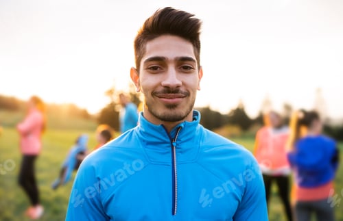 Preview: A portrait of young man with large group of people doing exercise in nature