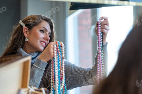 Preview: reflection of a woman in mirror choosing and trying different jewelry, soft focus, closeup
