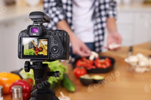 Preview: Food blogger cooking while recording video in kitchen, focus on camera