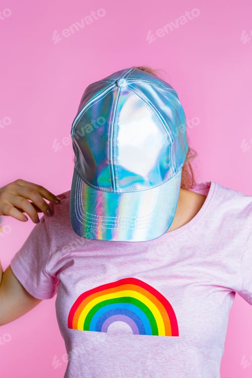 Preview: Young woman with headphones hiding her face behind basecap in front of pink background