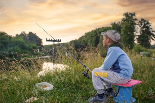 Preview: Young boy patiently waits for a bite, his gaze drawn to the mesmerizing sunset