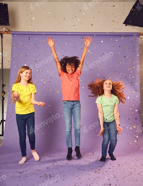 Preview: Studio Shot Of Children With Glitter Jumping In The Air With Outstretched Arms On Purple Background