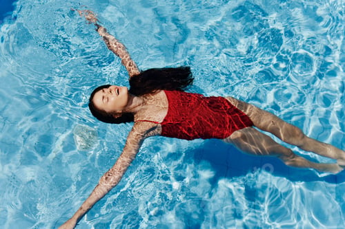 Preview: Happy woman swimming in the pool in red swimsuit with loose long hair relaxed in the sunshine, skin