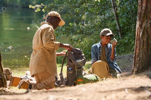 Preview: Aged African American man unpacking his rucksack while standing on knees